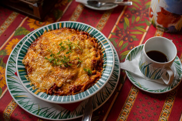 Healthy homemade mediterranean dish; spaghetti pasta with tomato sauce, overcooked cheese and thyme on top served in a bowl with cup of coffee on a table- selective focus