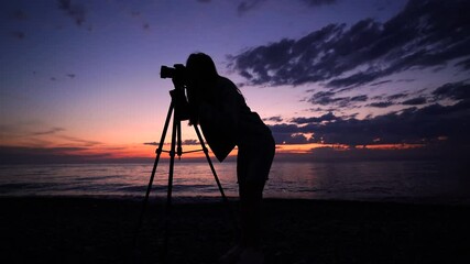 Silhouette of a woman traveler photographer taking a photo of nature and the sea with professional dslr camera on tripod - Powered by Adobe