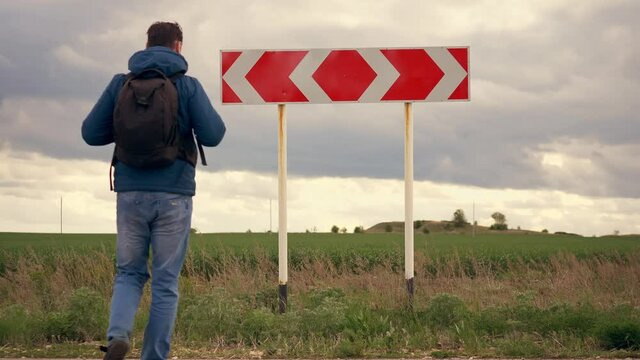 Choice of a way. Man tourist with a backpack comes up to the road direction sign and chooses the path. The problem of choice, decision making.
