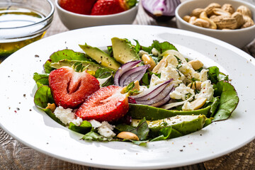 Fresh salad - feta cheese, avocado, lettuce, strawberries and onion on wooden table