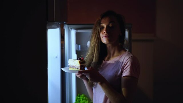 Young woman in the kitchen taking out a delicious sweet a piece of cake from the fridge and having a late night snack. Diet fail concept