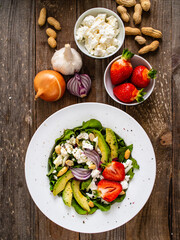 Fresh salad - feta cheese, avocado, lettuce, strawberries and onion on wooden table