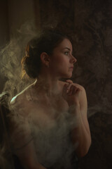 Creative portrait of a photo shoot using smoke a young beautiful girl with brown hair light falls on her hair