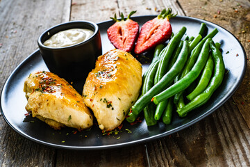 Roasted chicken fillets with green beans and strawberries on wooden table
