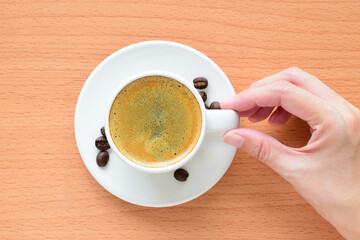 Hand holding espresso coffee cup on wooden table