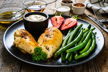 Roast chicken fillets with green beans and strawberries on wooden table
