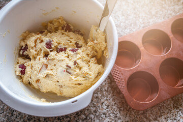 Muffinteig in einer weißen Schüssel mit Karamell, Kirschen und Schokolade. Daneben eine Muffin Backform aus Silikon. 