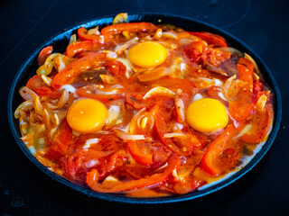 Shakshuka - fried eggs with chorizo and vegetables in frying pan
