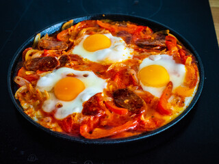 Shakshuka - fried eggs with chorizo and vegetables in frying pan
