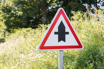 Junction warning road sign. Triangle shape. Sunny day in the countryside. Blurred background with green nature.