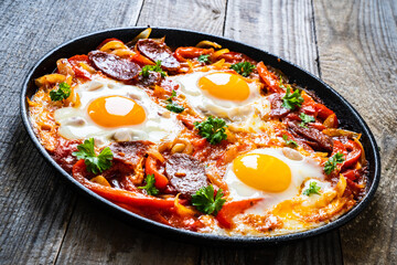 Shakshuka - fried eggs with chorizo and vegetables in frying pan
