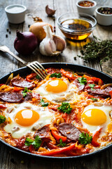 Shakshuka - fried eggs with chorizo and vegetables in frying pan
