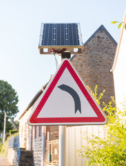 Turn left warning road sign supplied by solar energy through a solar panel. Sunny day in the countryside. Vertical shot.