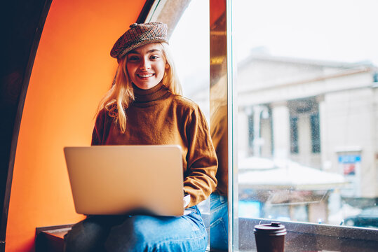 Portrait of cheerful female freelancer satisfied with successful online business working on free time in cafe, happy hipster girl enjoying studying via laptop computer sitting at coworking space.