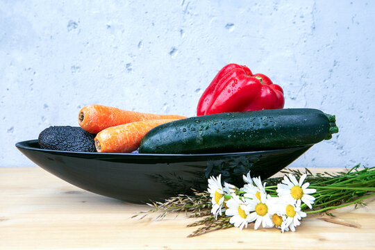 avocado, bell pepper, carrots and cougette in black bowl on wooden table with daisies