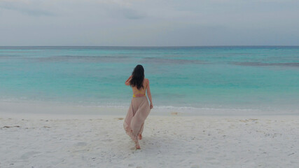 Fototapeta na wymiar young woman in long skirt walking towards the ocean. Tropical island on coral reef, Paradise of nature.