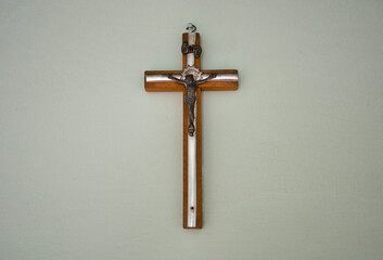 Small wooden / matal cross hanging on light pastel background in old vintage house