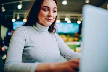 Positive female student watching tutorial for studying via laptop computer, skilled woman blogger...