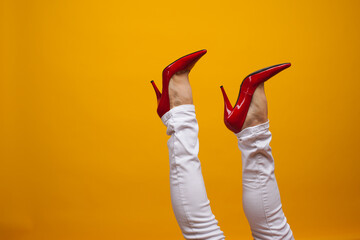 Female feet in beautiful red stiletto shoes, yellow background copy space.