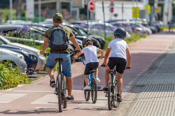 rear view of a man with children riding bikes on a bicycle path in the city, sunny day