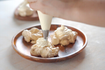the process of creating Pavlova dessert, decorating the meringue with cream from the culinary bag