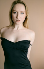 Fototapeta premium Graceful young woman in a black top posing against beige wall.