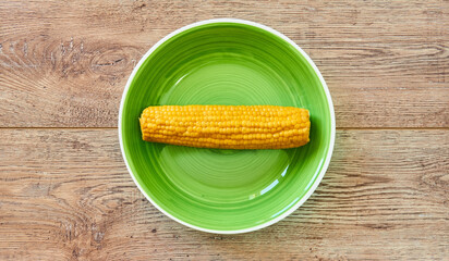 yellow cob of boiled cornon a green plate on a wooden tabletop