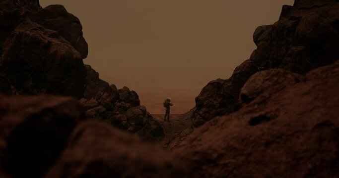 DOLLY IN Back view of lonely astronaut walking on a surface of a red rocky planet. Mars colonization concept. Dust effect added