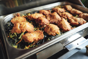 Stainless hotel pan on food warmer with fried meat and zucchini noodles. Self-service buffet table. Celebration, party, birthday or wedding concept.