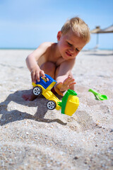 Little boy play at sea beach, dig and pour sand by plastic scoop to concrete mixer toy car, busy...