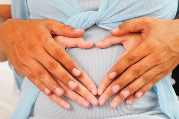 Father and mother putting their heart shaped hands together on growing baby bump expecting their cute baby at home Love and care and family lifestyle concept