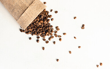 A burlap bag with coffee beans on a white, scuffed background. Concept of a popular invigorating drink. selective focus.