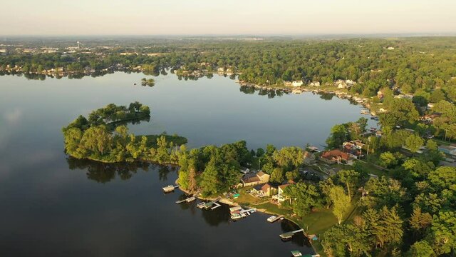 Aerial view of american suburb at summertime.  Establishing shot of american neighborhood. Real estate, residential houses with boat launch on the lake shore. Drone shot, from above, sunrise, morning