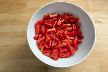 Sliced red bell peppers in a white bowl on a wooden kitchen table, healthy cooking with vegetables during the coronavirus pandemic, copy space, high angle view from above