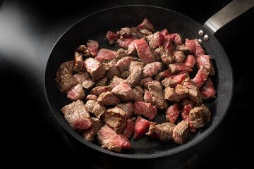 Roasting diced beef in a cooking pan on a black stove, preparation for goulash or stew, selected...