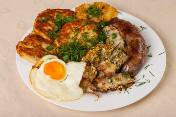 The plate with fried egg, fried sausage, bacon and potato pancakes. Closeup photo of Russian, Byelorussian and Ukranian hot main meal.