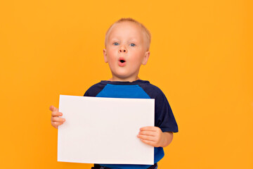 Happy boy with a smile holds a blank white sheet. Yellow background copy space