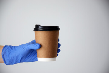 Hand holds cardboard cup of coffee with empty space for text on gray background. Coffee shop or delivery service. Copy space.