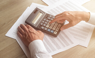 Hands of businessman doing finances and calculate on desk about cost. Concept finances and economy. tables with digits on wooden desk and male hand pressing the button on calculator