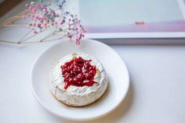 Camembert cheese baked with berry sauce on the background of the magazine. Light daylight