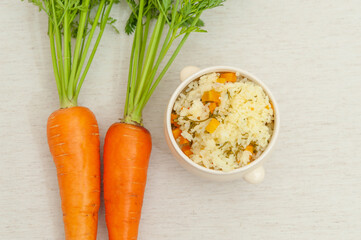 Vegetarian / vegan cuisine - Raw carrots with leaves and a bowl of cooked rice with carrots. Isolated on white background. Copy space. Top view. Horizontal shot.