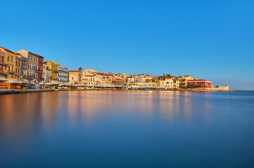 Fototapeta na wymiar View of old harbor of Xania of Crete island Greece. Taverns on the pier in the rising sun with slow motion effect water in the foreground. Bay of Xania on sunny summer day. 