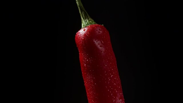 Close-up view to rotating red chili pepper with water drops. Cayenne isolated on black background. High quality footage. 4k