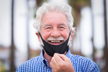 Portrait of smiling senior man with white hair wearing facial mask due to coronavirus - new normal...