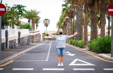 Deserted street due to coronavirus with senior woman in the middle of road wearing facial mask -...