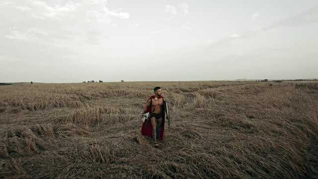 Shirtless spartan walking in dry field.