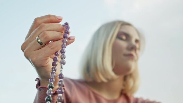 Hand of young believing woman prays in nature and uses craft rosary beads to count prayer and concentrate on meditation. Religion, hope, love concept. Slow motion.