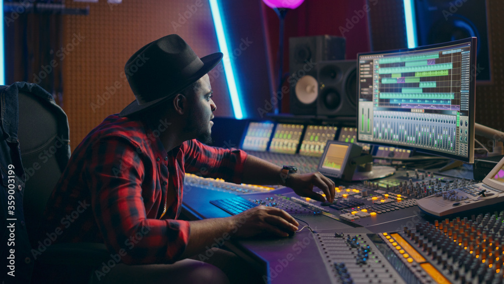 Poster stylish male audio engineer working in music recording studio, uses mixing board, software to create