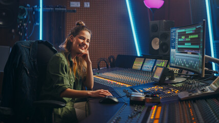 Stylish, Beautiful Female Audio Engineer Working in Music Recording Studio, Uses Mixing Board Create Song. Looking at Camera Portrait of a Girl Artist Musician Working at Control Desk and Smiling - obrazy, fototapety, plakaty