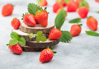 Fresh raw organic summer strawberries with a lot of vitamins and leaf on round timber boards on light background.